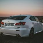 Stylish white Lexus IS parked on an empty road under a dramatic sunset sky.